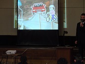 自転車での道路横断について、場所の写真をスクリーンに映して話しています。