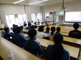 階段状に机が配置された講義室で話を聞く子どもたち。